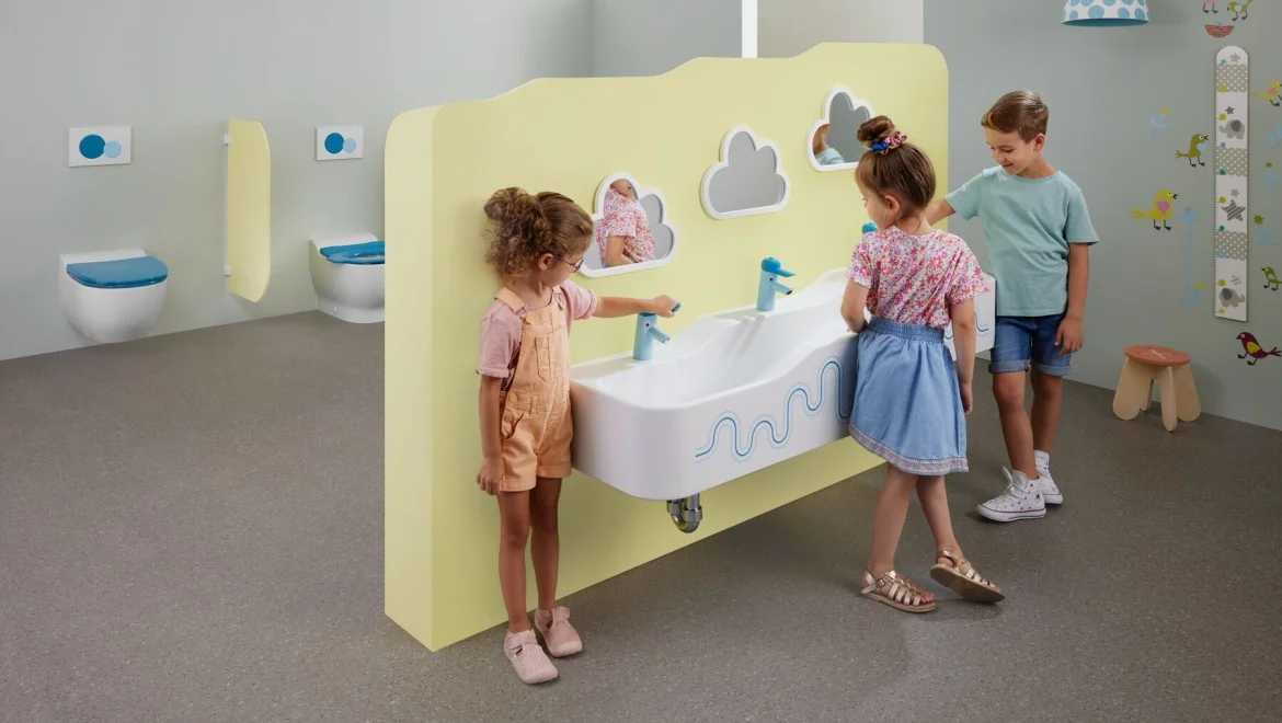 Enfants devant un espace de lavage Geberit Bambini dans des sanitaires adaptés.